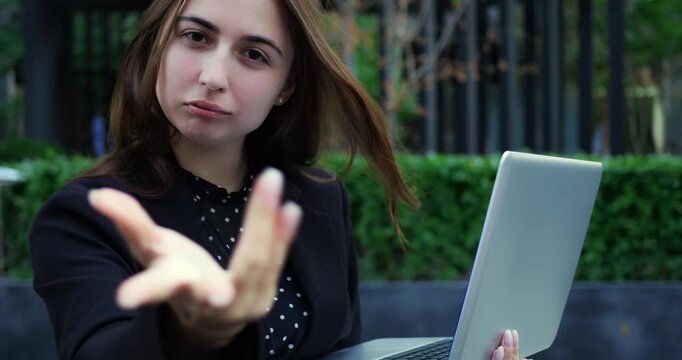 Caucasian woman outdoor closing laptop, blazer and polka blouse, assertive swipe and dismissive facial expression, urban courtyard environment, brief frustrated gesture during hybrid work routine