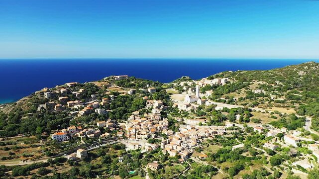 Scenic aerial shot of Corbara village nestled in the hills overlooking the deep blue Mediterranean Sea in Corsica, France, on a clear sunny day.