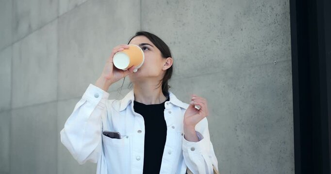 Relaxed woman drinking. Woman enjoys coffee outdoors. Calm woman with shopping bags drinking coffee peacefully. Tranquil woman with paper cup and shopping bags pauses amid city errands