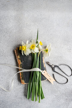 Overhead view of a bunch of daffodils tied with a ribbon and a gift tag with the words thank you on top of an old book next to a pair of scissors