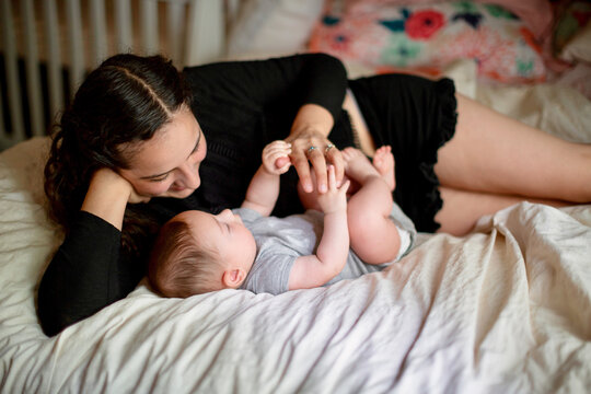Young woman lying on her side on a bed playing with her young son
