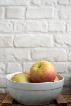 Close-up of a four Apples in a bowl on a table by a white brick wall