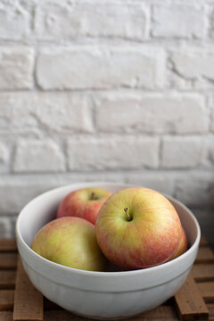Close-up of a four Apples in a bowl on a table by a white brick wall