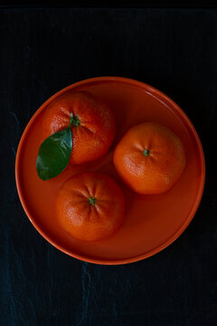 Overhead view of three tangerines on an orange plate on a black background