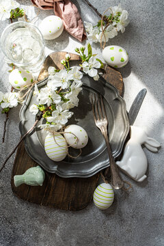 Overhead view of a rustic spring place setting with cherry blossoms on a pewter plate, assorted Easter decorations and a glass of water on a table