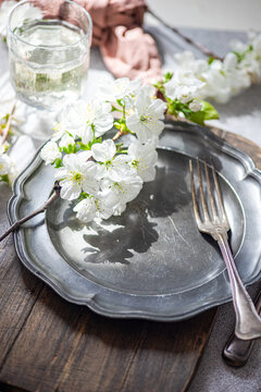 Close-up of a rustic spring place setting with cherry blossoms on a pewter plate and a glass of water