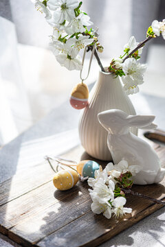 Close-up of a Spring table setting with a vase of cherry blossoms with assorted Easter ornaments on a wooden chopping board