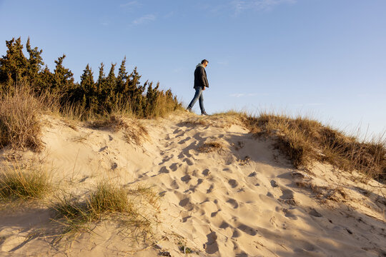 Man walking alone on sandy dune under clear blue sky