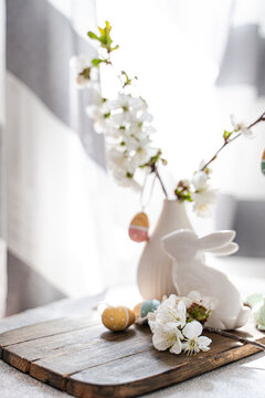 Close-up of a Spring table setting with a vase of cherry blossoms with assorted Easter ornaments on a wooden chopping board