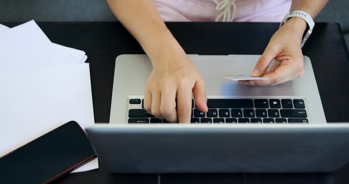 Lady enters credit details carefully. Female individual verifies payment information on computer. Woman carefully enters her credit card details into computer while reviewing paperwork