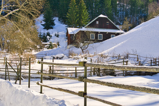 View of a rustic wooden house nestled amidst snow-covered hills, a serene winter landscape punctuated by bare trees and a weathered wooden fence, Moce, Banska Bystrica Region, Slovakia.