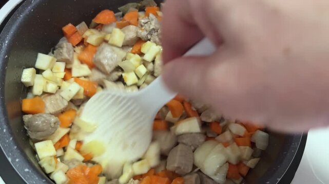 Stirring meat with vegetables in multi-cooker during goulash cooking