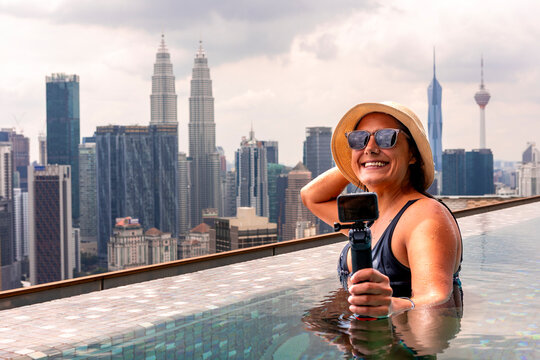 Woman filming in rooftop infinity pool with Kuala Lumpur view