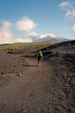 Lone hiker trekking on volcanic trail toward snowy peak