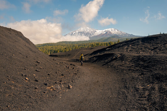 Hiker on volcanic trail with snowy mountain in distance