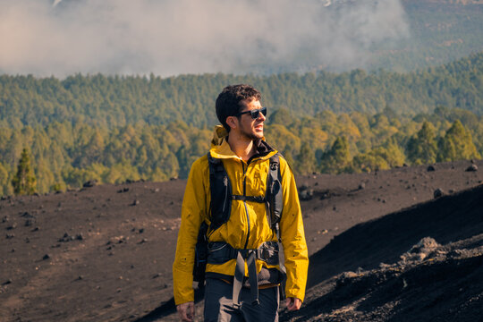 Hiker in yellow jacket on volcanic trail above forest