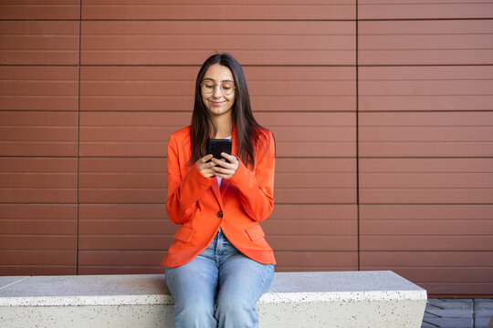 Woman in orange jacket using smartphone outdoors