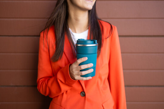 Woman in orange blazer holding a reusable coffee cup