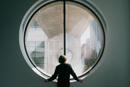 Person looking out round window at modern city buildings