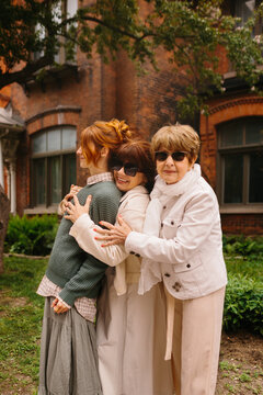 Multi generational women hugging outside brick building