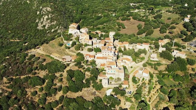 Scenic aerial shot of the picturesque hilltop village of Pigna surrounded by lush greenery in Corsica, France. Traditional Mediterranean houses with terracotta roofs nestled in a rural landscape.