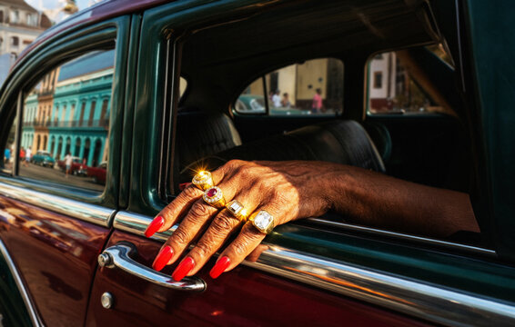 Hand with red nails and rings resting on vintage car door