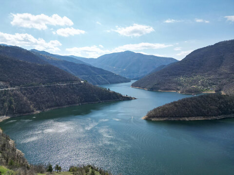 A calm river a winding riverbed a reservoir dark water a deep canyon with steep slopes a deciduous forest with spring greenery the nature of the Rhodope Mountains the Balkans
