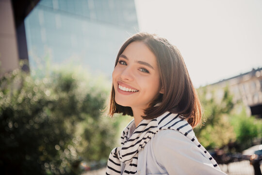 Smiling young woman portrait outdoors in city enjoying a sunny day, casual style with striped scarf and a confident relaxed expression