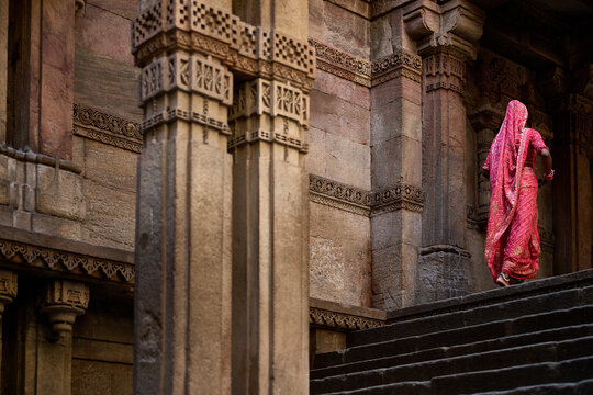 Woman in traditional pink sari walking up stone steps past carved pillars at Adalaj Stepwell, Ahmedabad, Gujarat, India, Asia.
