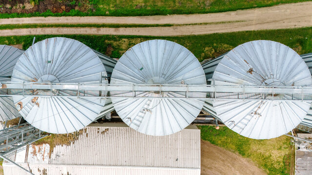 Aerial view of silver silos gleaming under the sun, standing tall against the backdrop of verdant fields and a sandy path, Sremska Mitrovica, Vojvodina, Serbia.