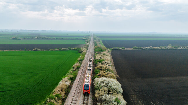 Aerial view of a vibrant red train slicing through the heart of the country, flanked by contrasting green and brown fields, Sremska Mitrovica, Vojvodina, Serbia.