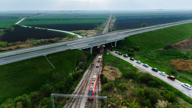 Aerial view of a long train passing under a highway bridge, contrasted against the dark fields under a cloudy sky, Sremska Mitrovica, Vojvodina, Serbia.