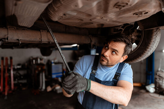 Mechanic works on car underbody using tools in garage during daytime