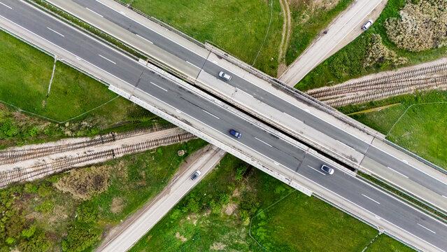 Aerial view of a highway interchange with vehicles cutting through lush green fields, a modern intersection of concrete and nature, Sremska Mitrovica, Vojvodina, Serbia.