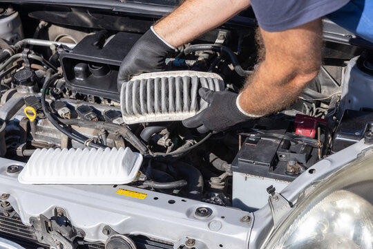 Mechanic replacing dirty engine air filter with clean new filter during car maintenance service inspection