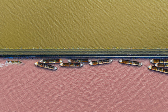 Aerial view of boats floating on the pink waters contrasting sharply with the yellow waters, separated by a thin strip of land, San Pedro del Pinatar, Region of Murcia, Spain.
