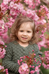 Fototapeta premium Smiling girl with cherry pink blossoms standing outdoors in spring, happy childhood scene, natural beauty, carefree emotion, springtime festivity.