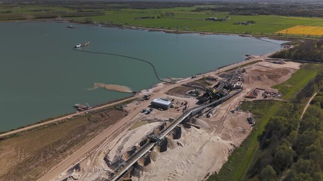 Wide aerial orbit of active sand quarry and processing plant beside a lake