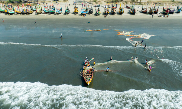 Aerial view of vibrant fishing boats lining the sandy beach as fishermen cast their nets into the sea at Cox's Bazar, Chittagong Division, Bangladesh.