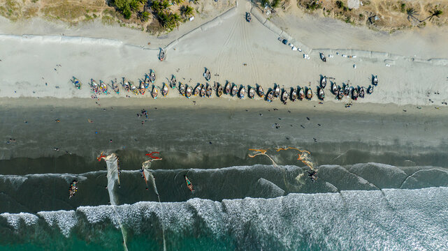 Aerial view of boats lined up on the sandy beach, with gentle waves lapping the shore, creating a mesmerizing contrast of textures and tones, Cox's Bazar, Chittagong Division, Bangladesh.