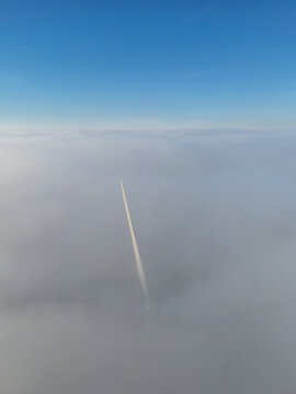 Aerial view of a solitary contrail slicing through an endless expanse of clouds under a serene blue sky, Chateaudun, France.
