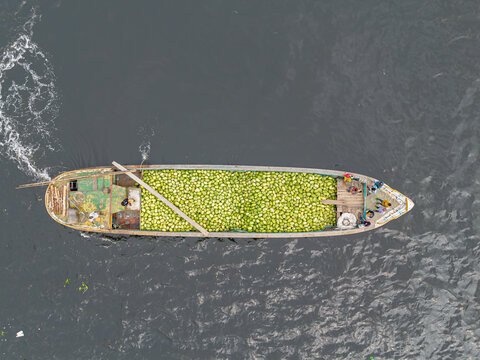 Dhaka, Bangladesh - 04 April 2026: Aerial view of a boat brimming with light green gourds sailing on the dark waters of the river, creating a striking contrast.