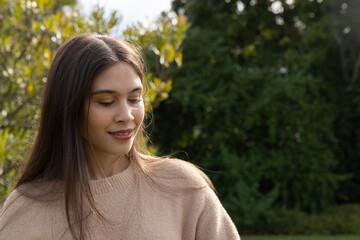 Naklejka premium Adult female standing in garden with long hair wearing beige knit sweater facing shrubbery hedge
