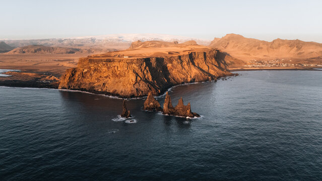 Aerial view of basalt sea stacks of Reynisdrangar rise dramatically from the dark, churning ocean waters, framed by rugged cliffs, Reynisdrangar, Iceland.