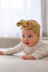 Fototapeta premium Adorable baby girl with a mustard yellow bow on her head lying on her stomach