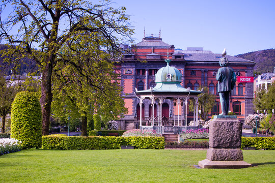 View of a statue standing proudly in a park with a bandstand, set against the backdrop of a grand brick building, West Old Town, New Mexico, Sweden.
