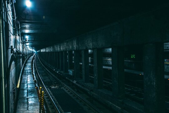Dark subway tunnel with curving tracks, a mysterious underground passage. Moody urban infrastructure, a long, dimly lit metro railway for transport and travel.