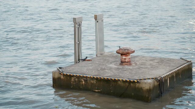 Concrete mooring platform floating on water, weathered bollard with rust and barnacle growth, small gull perched on edge, gentle ripples reflecting soft evening light, industrial waterfront vibe
