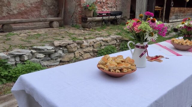 Static shot of traditional wedding table setup with pastries and flowers, featuring musical instrument cases in the background, in the UNESCO village of Vlkol&iacute;nec, Slovakia.