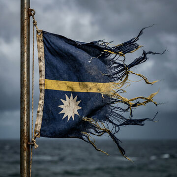 Tattered nauruan flag waving on a flagpole near the sea under a cloudy sky with national flag island nation state emblem national pride flag day tattered distressed weathered flagpole